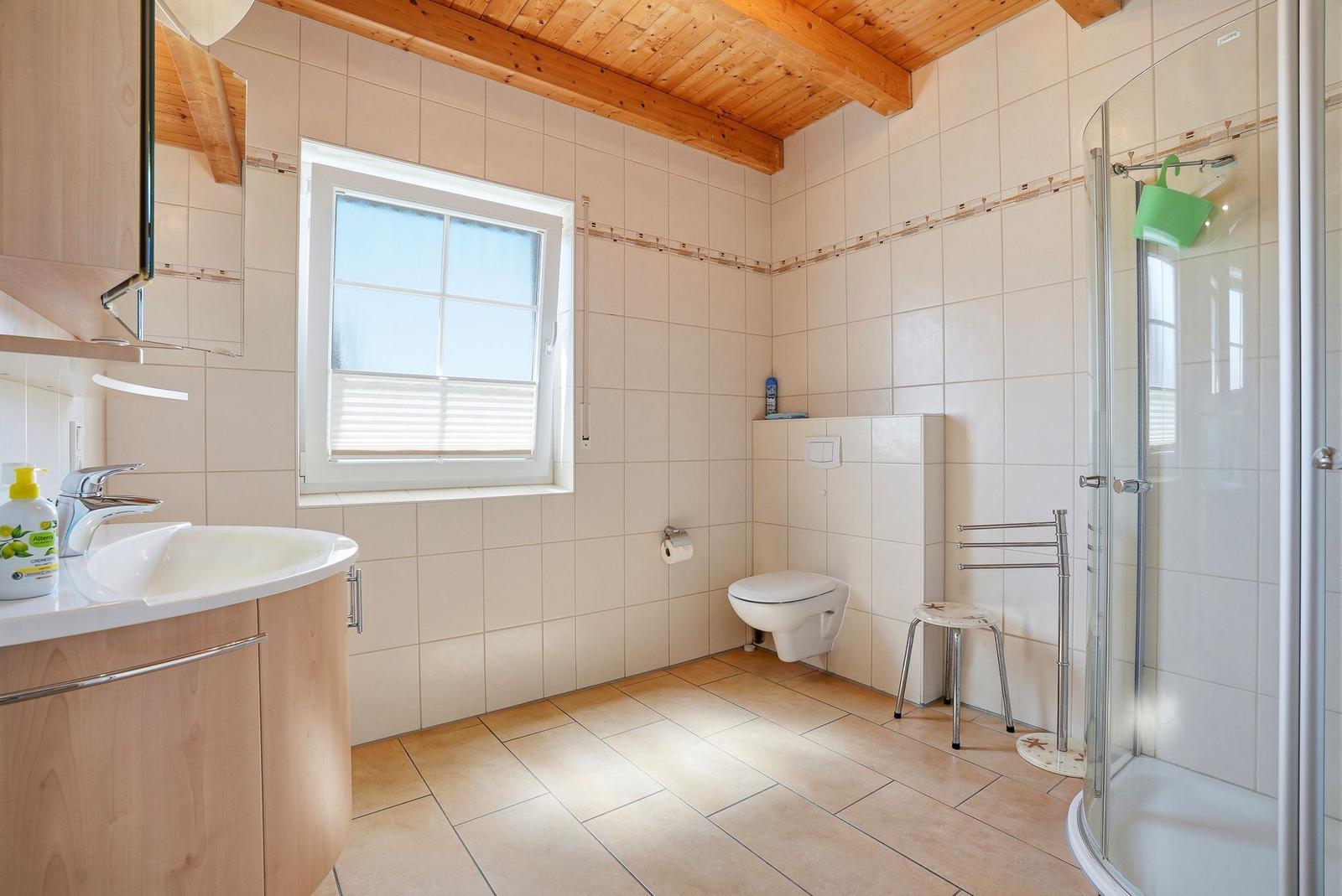 Badezimmer mit Dusche, Toilette und Waschbecken unter Holzbalkendecke.