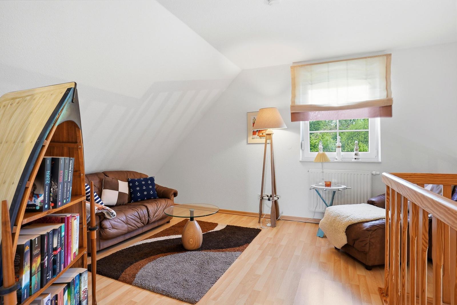 Wohnzimmer mit Sofa, Bücherregal und Fenster mit Blick auf Grün.