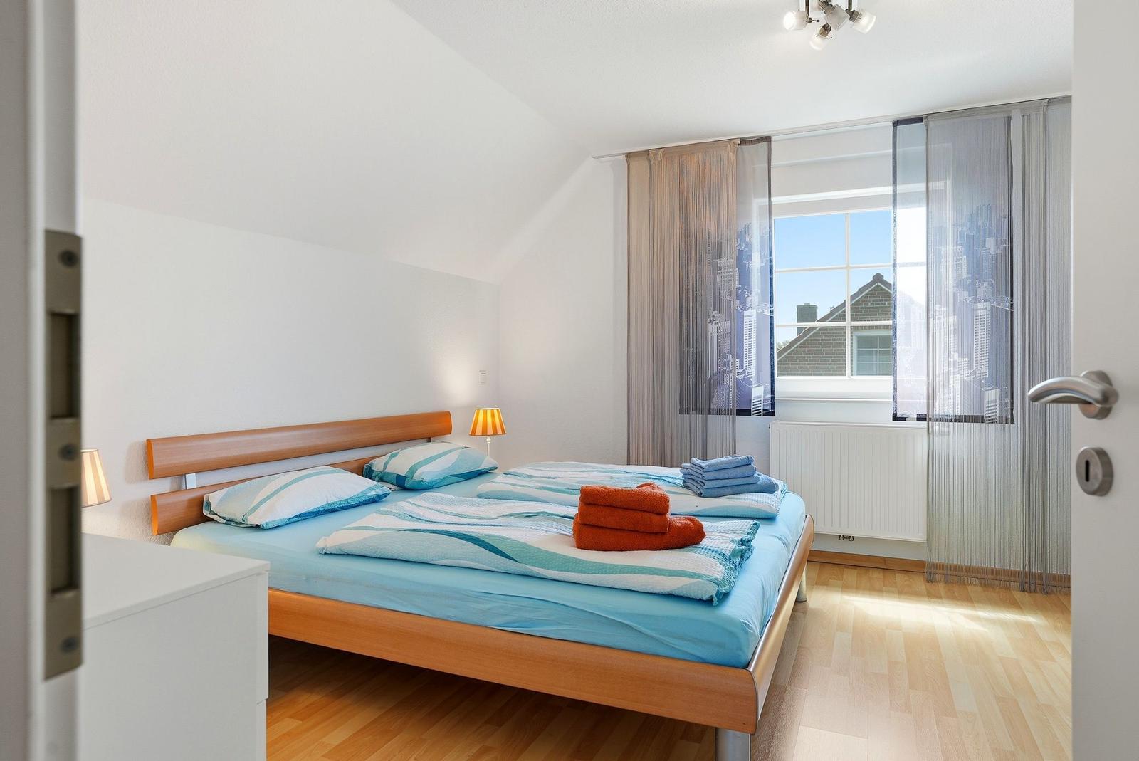 Schlafzimmer mit Doppelbett, Holzboden und Fenster mit Vorhängen.