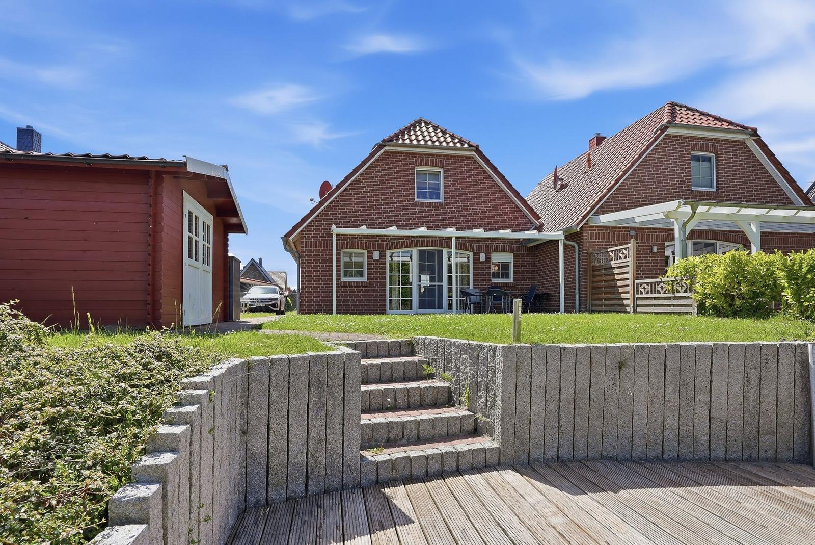 Haus mit Terrasse und Garten. Holzterrasse, Steintreppe und rote Ziegelmauer.