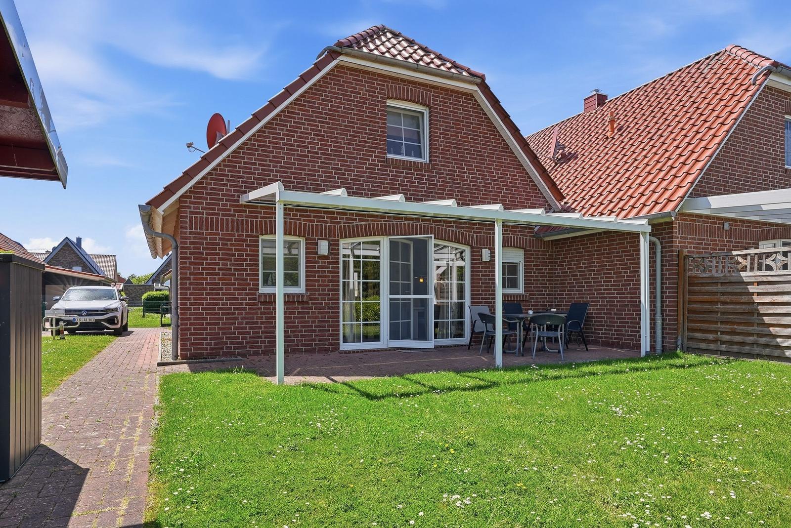 Rotes Ziegelhaus mit Terrasse und Garten. Tisch und Stühle stehen unter einem Dach.