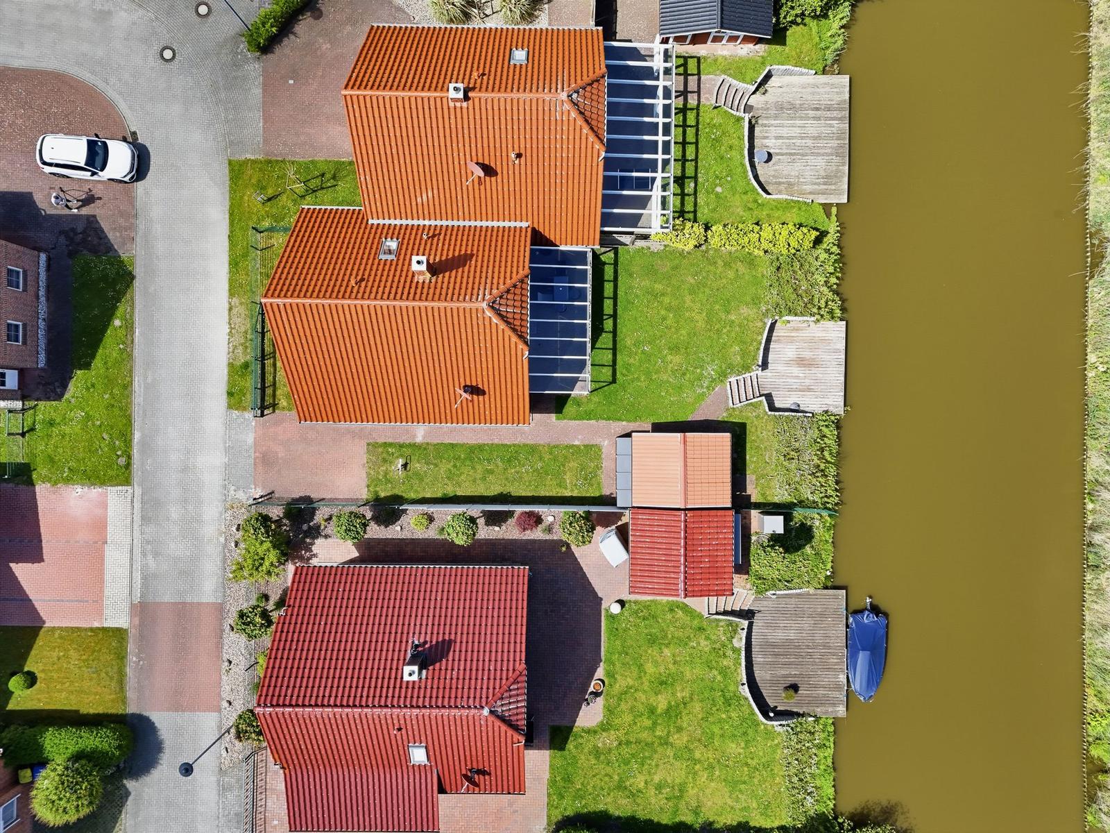 Haus mit rotem Dach, Garten und Bootssteg am Wasser.