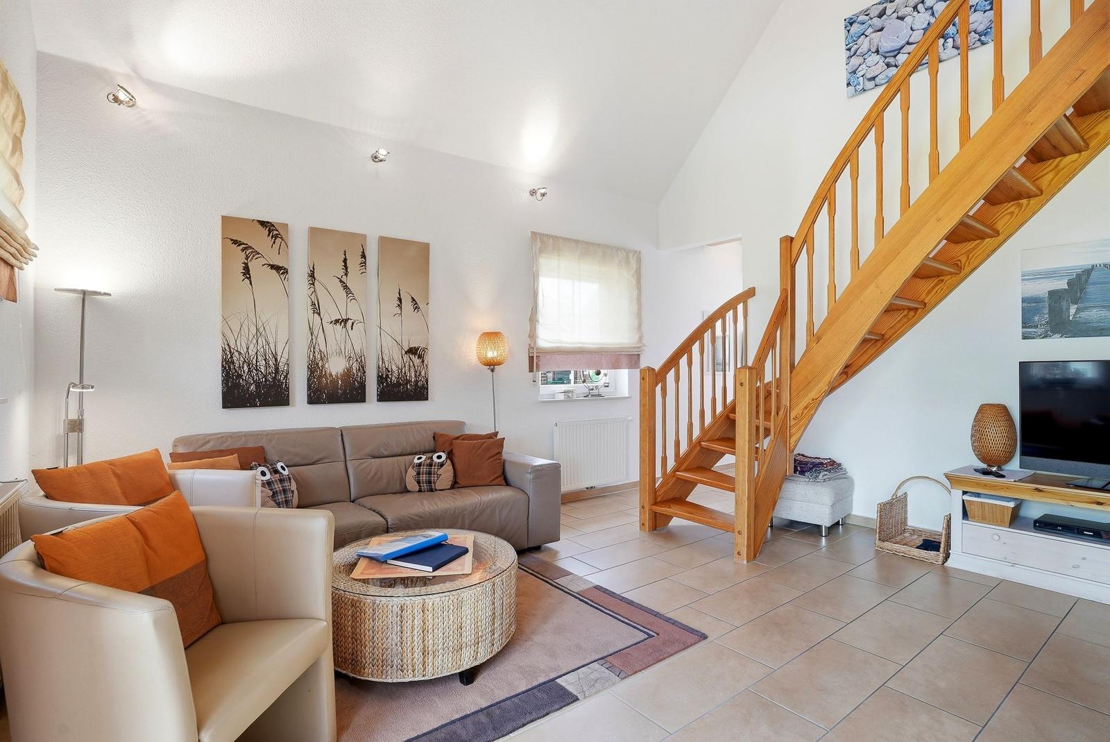 Wohnzimmer mit Sofa, Sessel, Couchtisch und Holztreppe.
