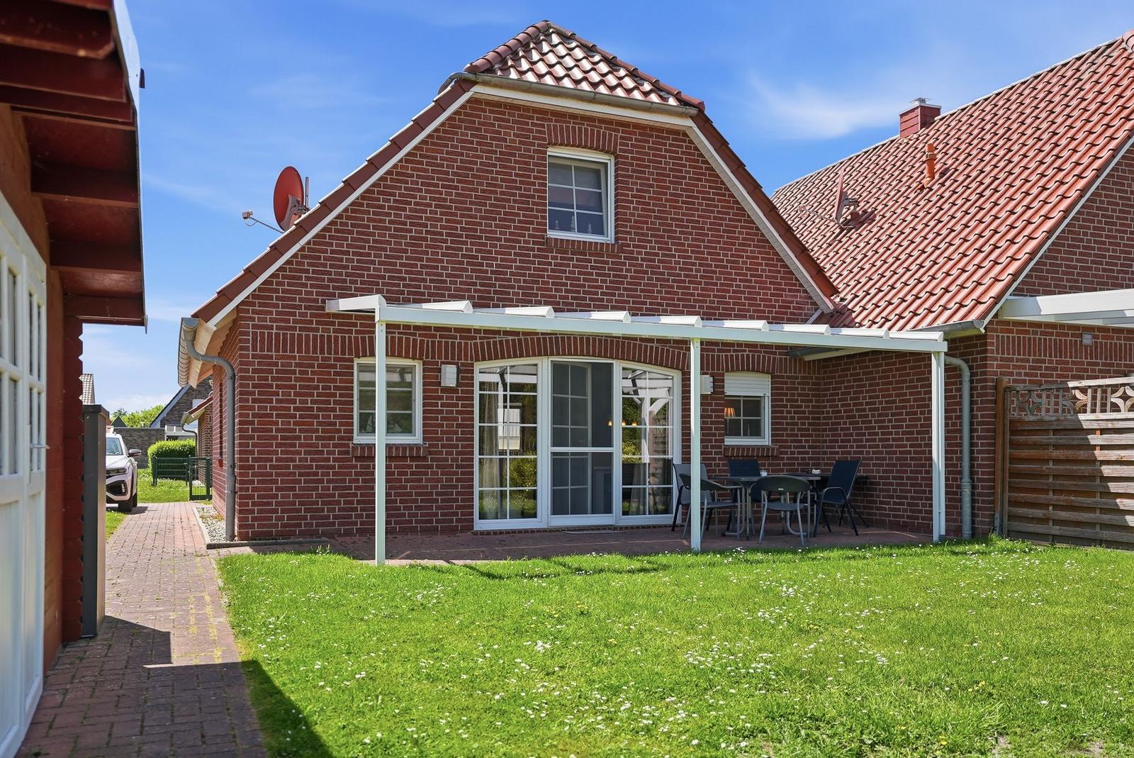 Rotes Backsteingebäude mit Terrasse und Garten. Glastüren führen auf die Außenterrasse.