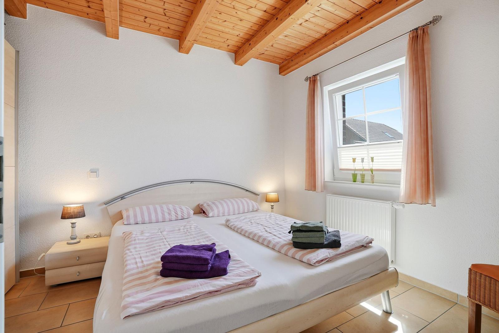 Schlafzimmer mit Doppelbett, Holzdecke und Fenster mit Vorhängen.