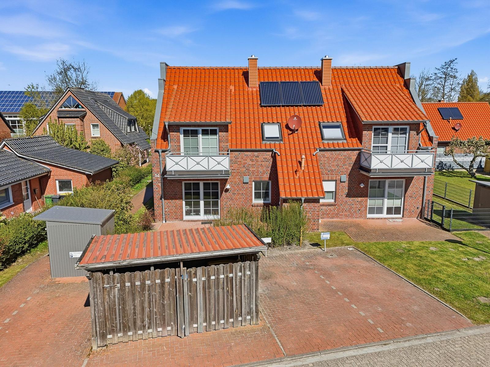 Rotes Dach mit Solarpanel, zwei Balkone, Holztor und gepflasterter Hof.