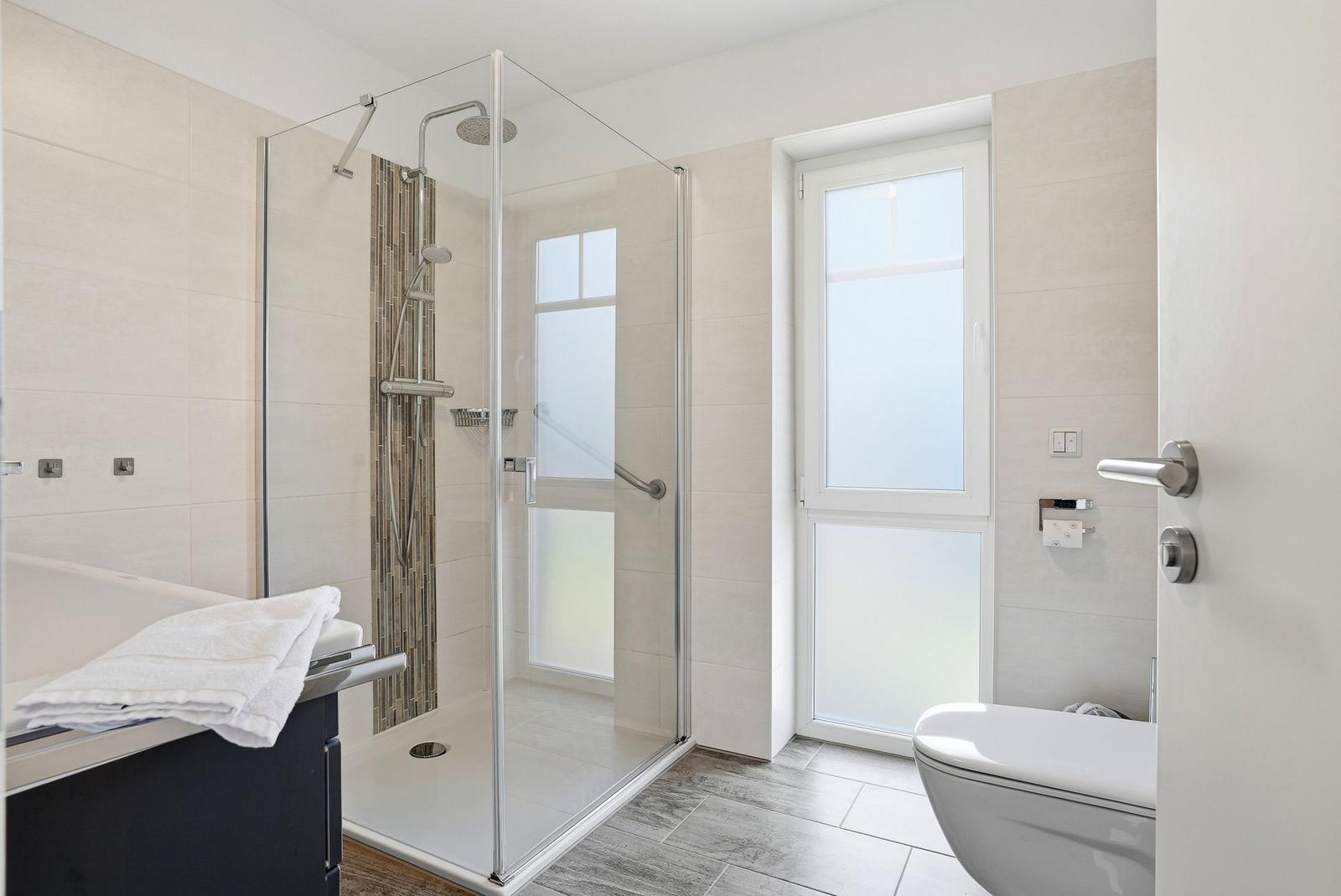 Dusche mit Glaswand, Toilette und Waschtisch in moderner Badezimmerausstattung.