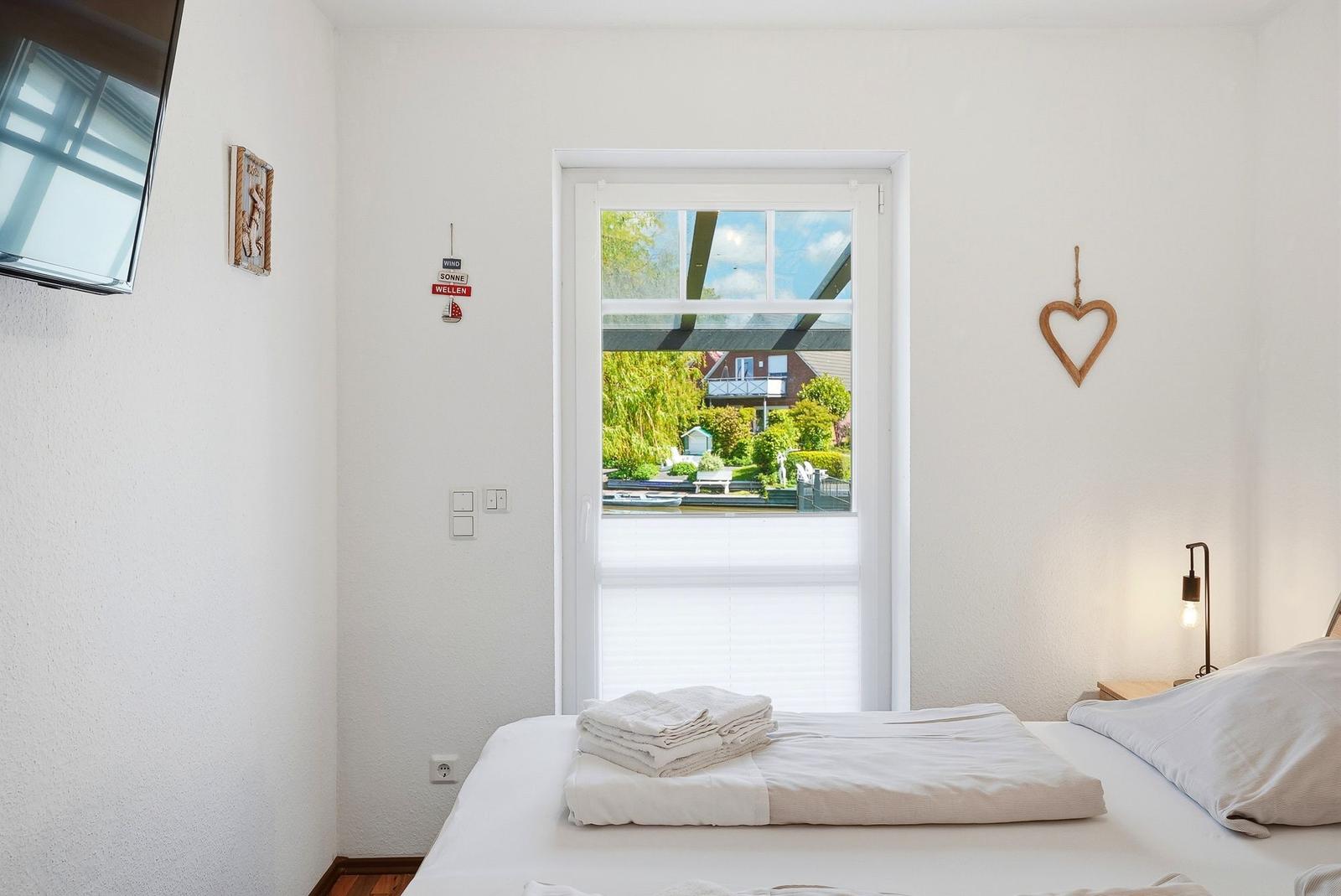 Schlafzimmer mit Blick auf den Kanal und Garten. Bett, TV und Wanddekoration.