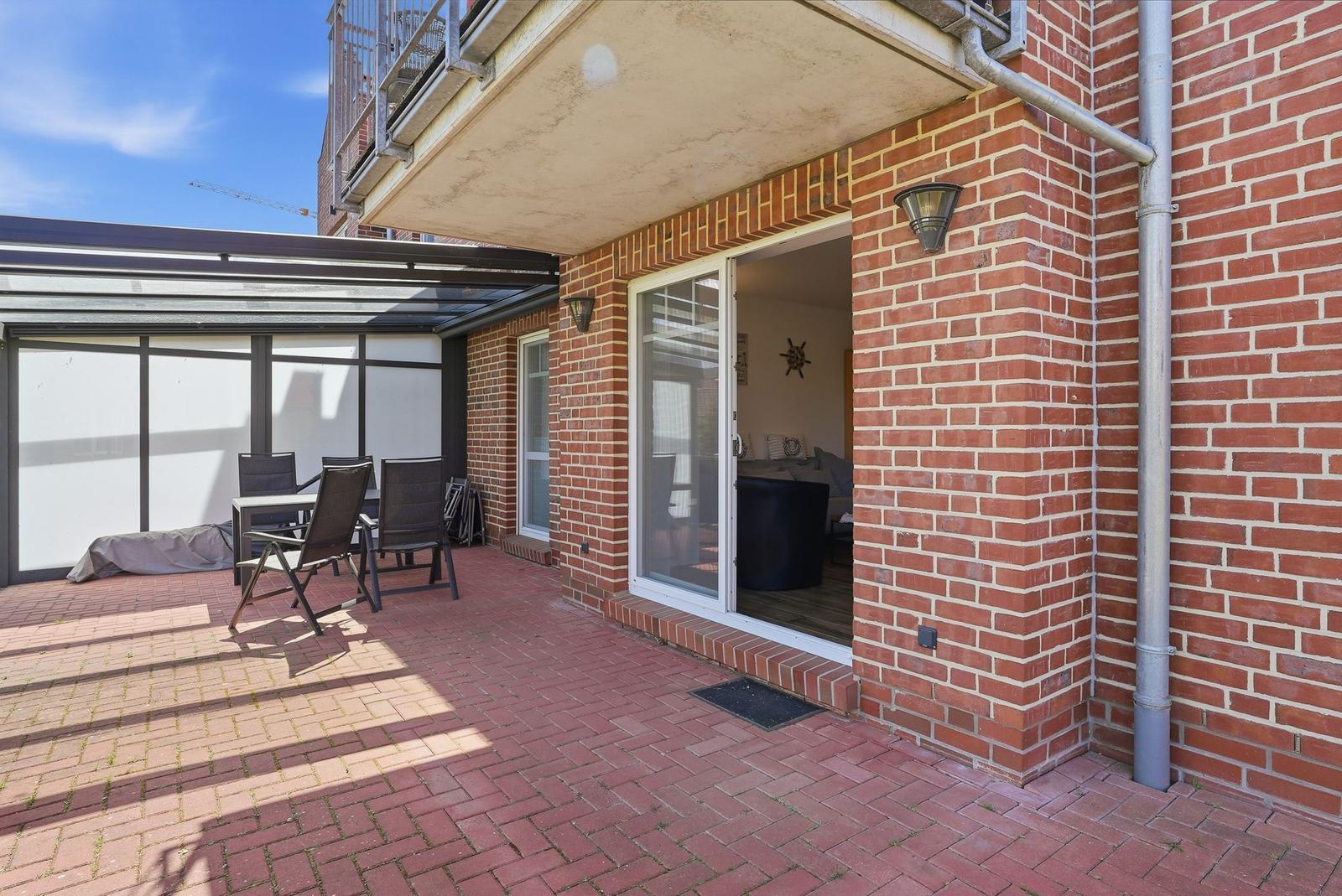 Terrasse mit Sitzgelegenheit und Zugang zum Haus. Roter Ziegelboden und Backsteinmauer.