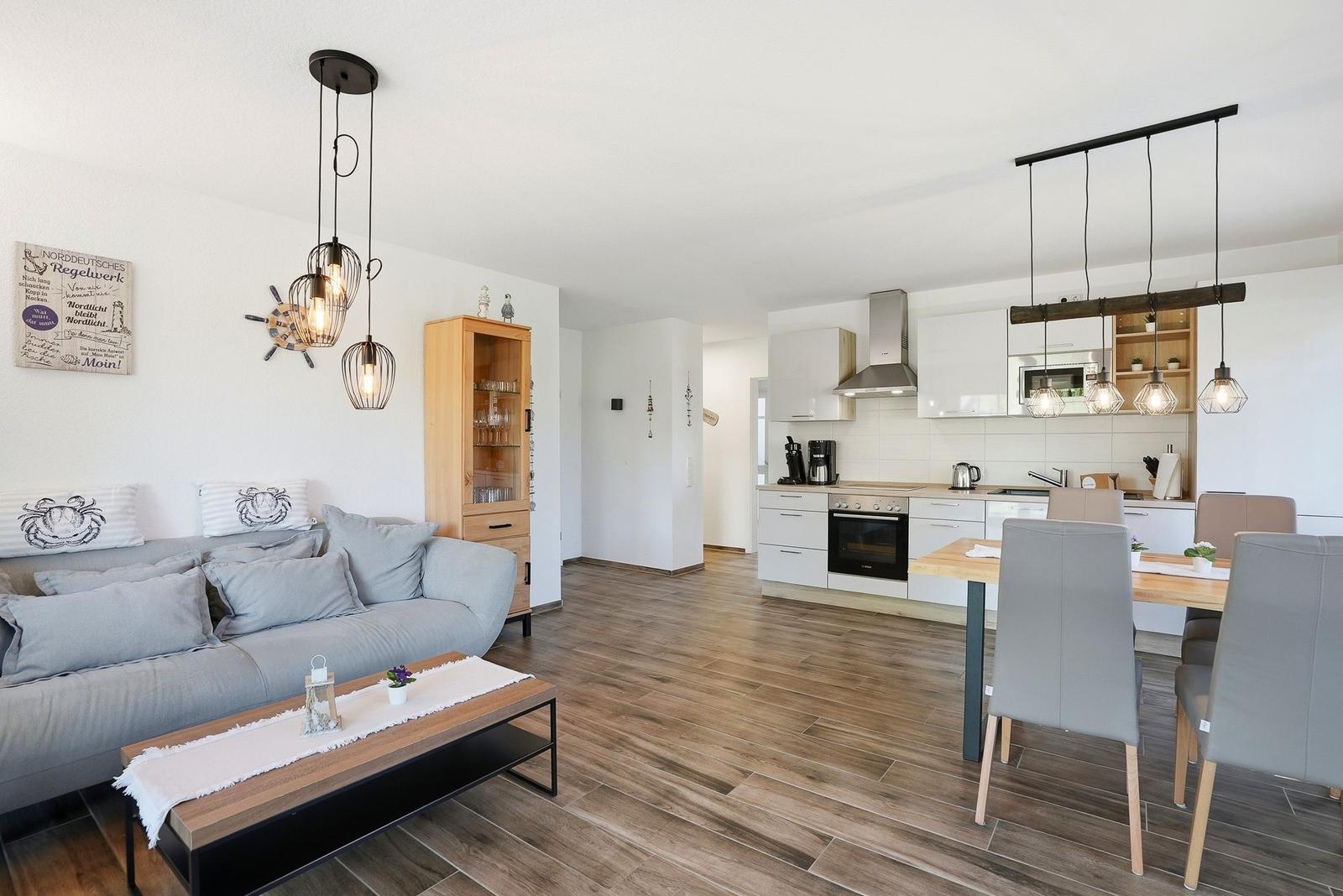 Wohn- und Küchenbereich mit Holzboden, Sofa, Esstisch und moderner Küchenzeile.