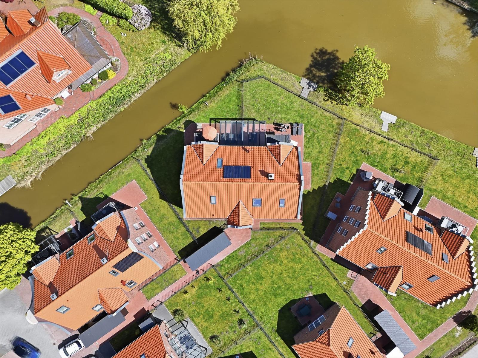 Haus mit rotem Dach und Terrasse an Kanal mit grünem Rasen.