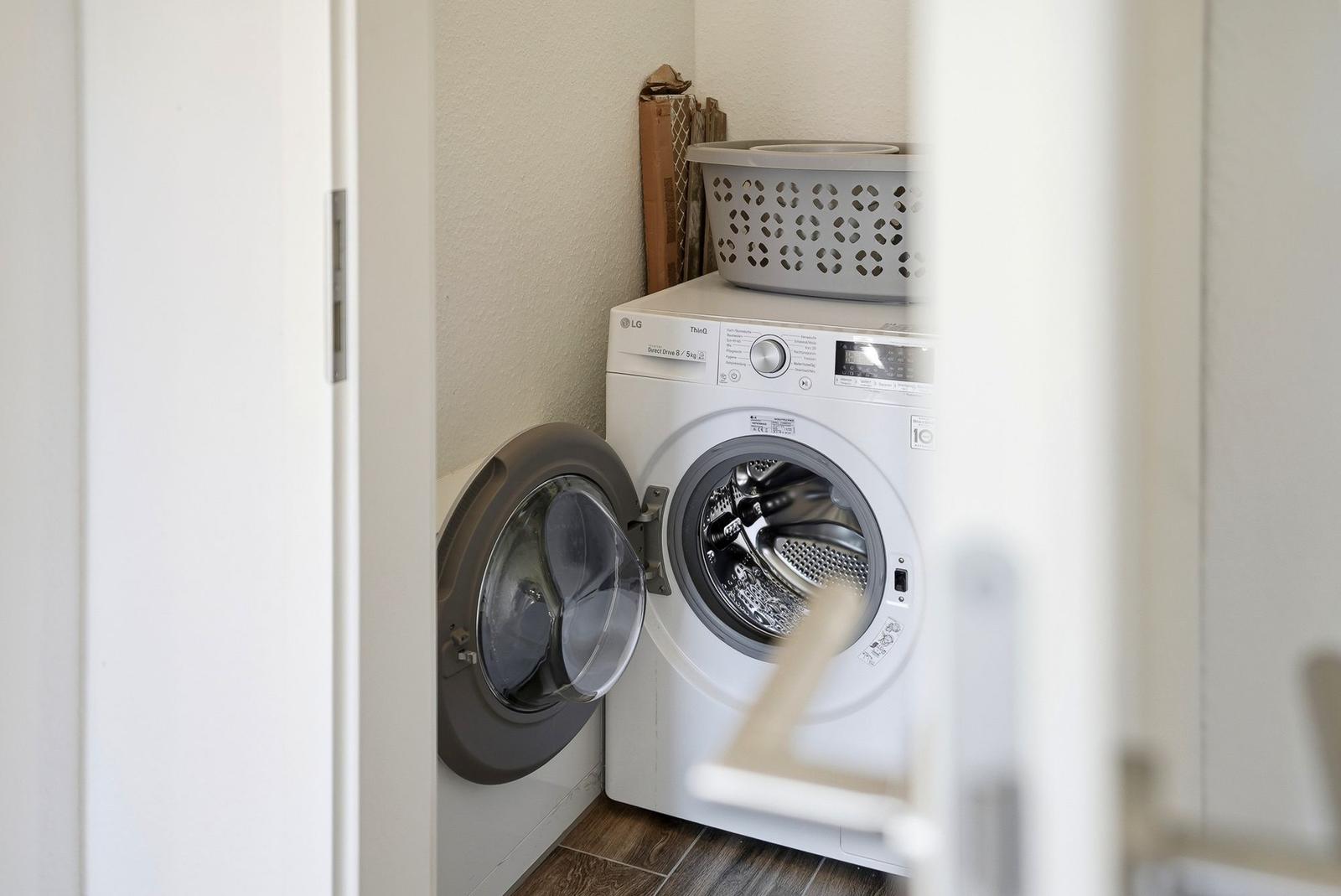 Waschmaschine in einem Raum mit Holzboden und Korb.