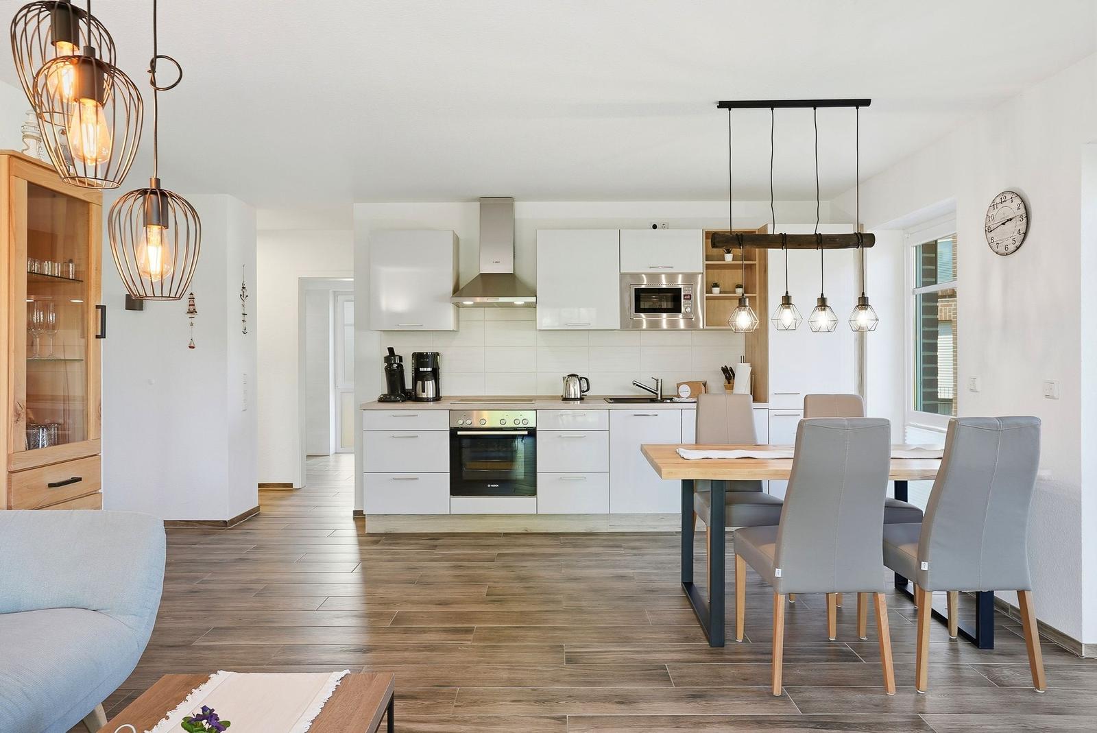 Küche mit Essbereich, weißen Schränken, Holzfußboden und moderner Beleuchtung.