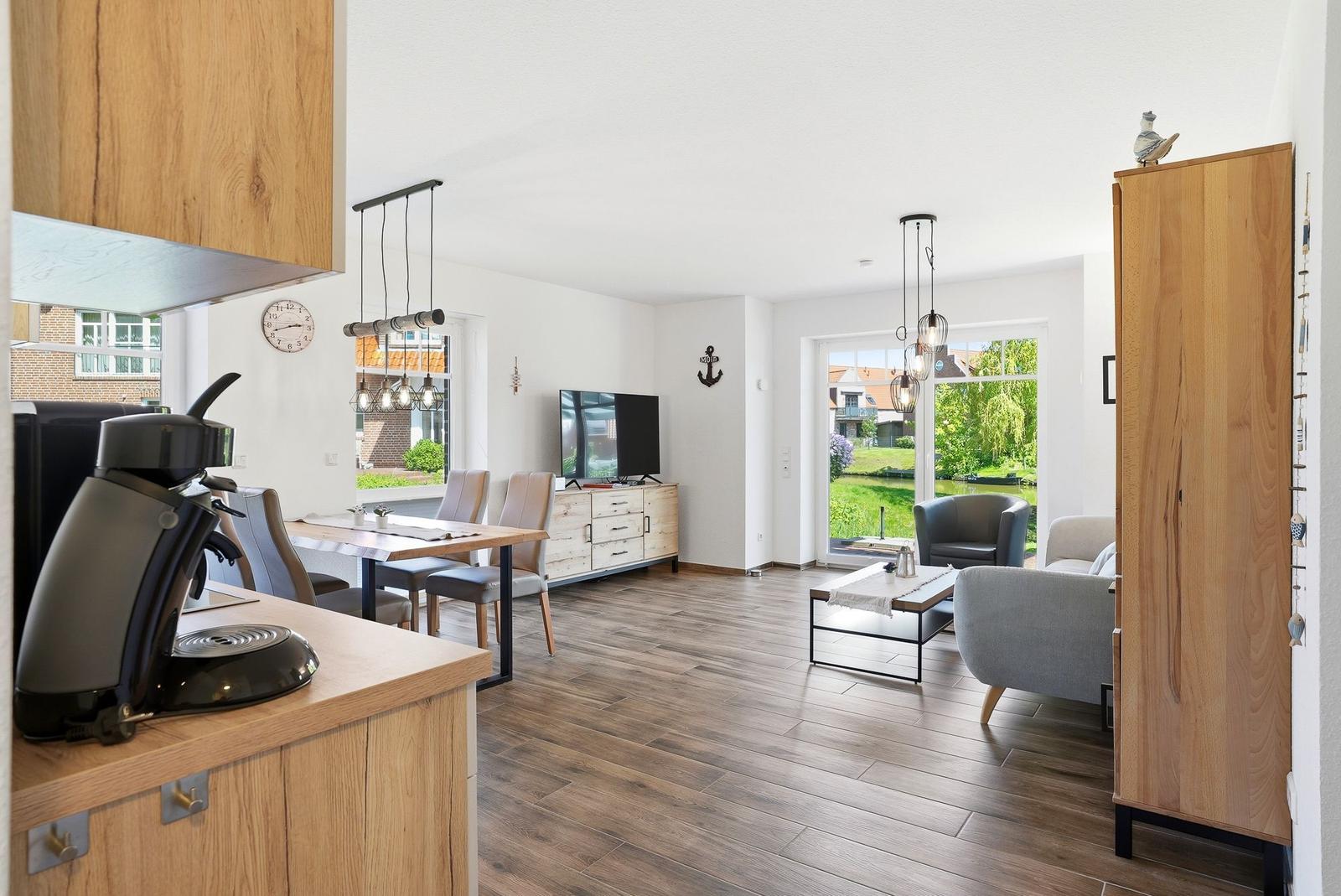 Wohn- und Essbereich mit Holzboden, TV, Tisch und Stühlen sowie Blick auf einen Garten.