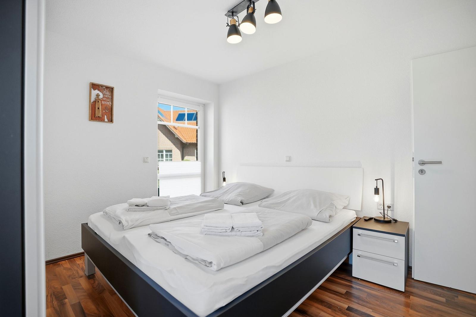 Schlafzimmer mit Bett, Nachttisch und Fenster. Holzboden und Wandbild.