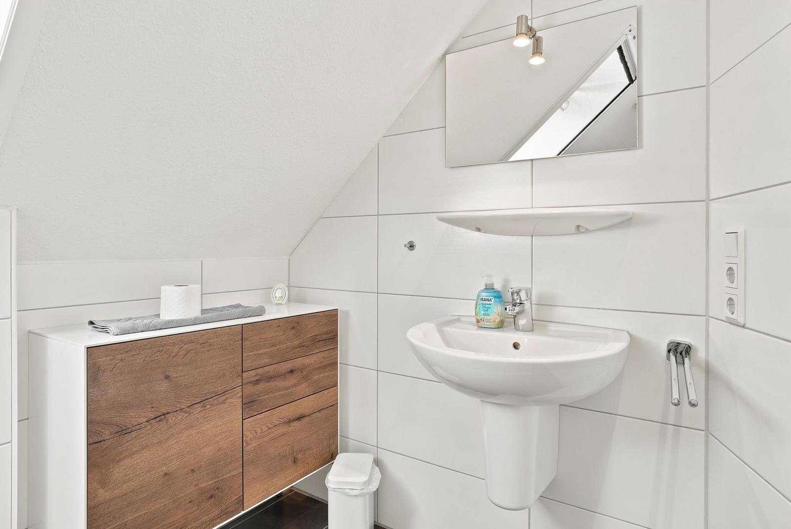 Badezimmer mit Waschbecken, Spiegel und Holzschrank unter Dachschrägen.