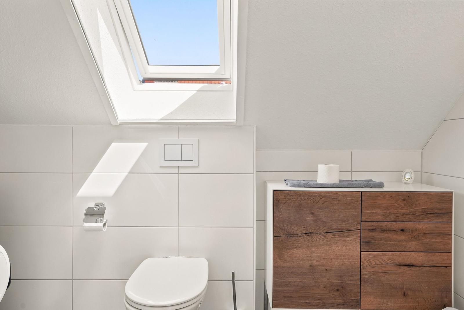 Badezimmer mit Toilette, Holzschrank und Dachfenster.