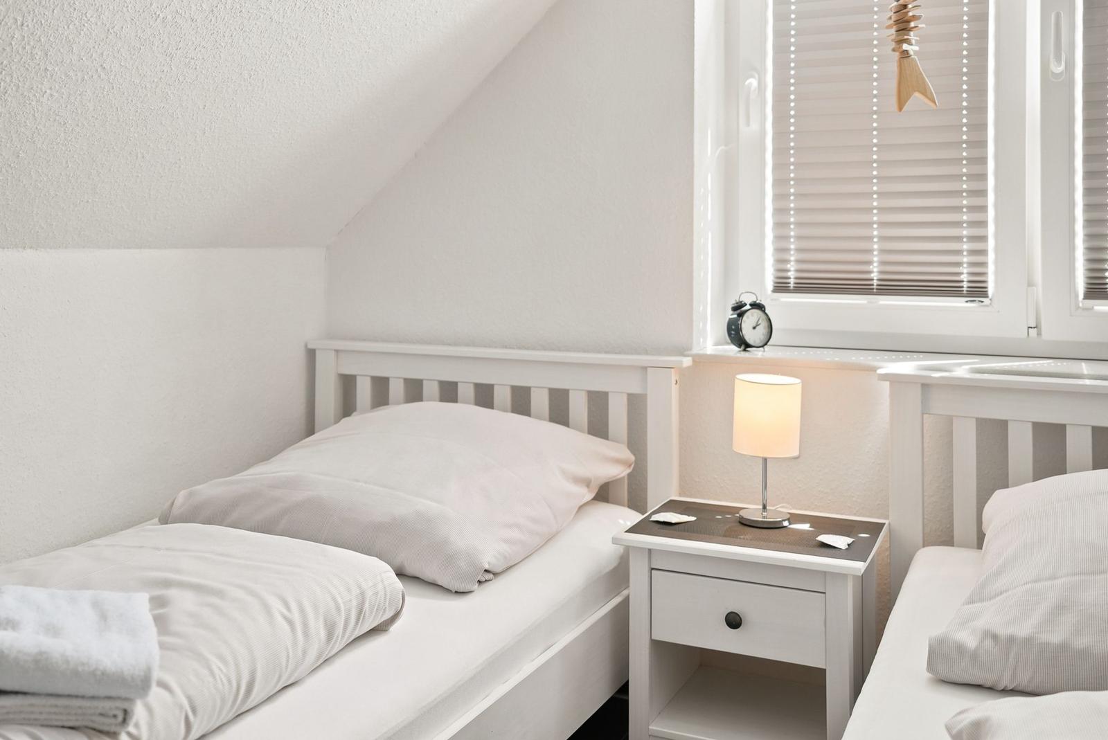 Zimmer mit zwei Betten, Nachttisch und Fenster mit Jalousie.