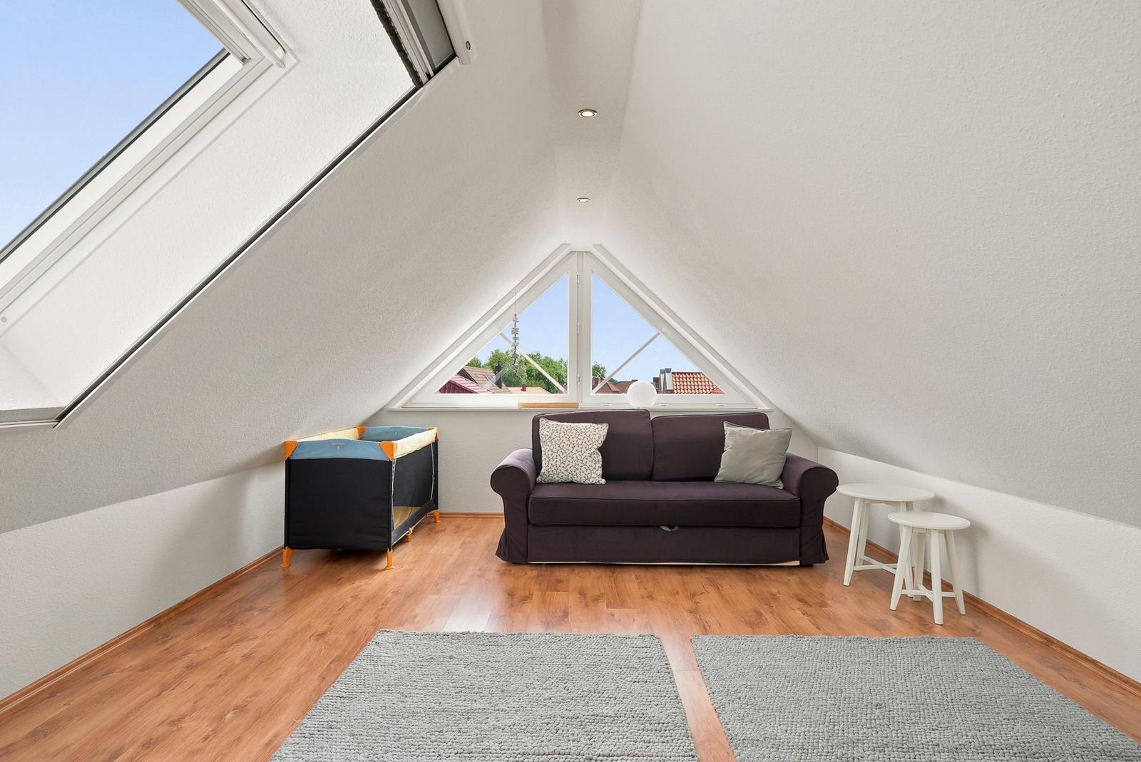 Dachgeschosszimmer mit Sofa, Kinderbett und großen Fenstern.