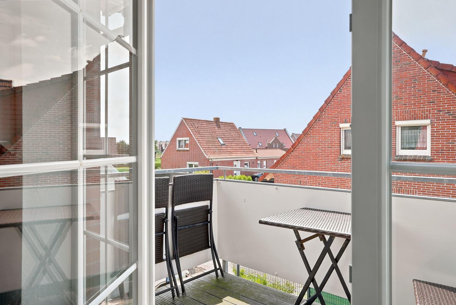 Balkon mit Tisch und Stühlen, Blick auf rote Dächer und Himmel.
