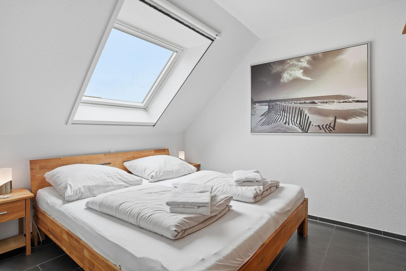 Schlafzimmer mit Dachfenster, Bett, Nachttisch und Wandbild.