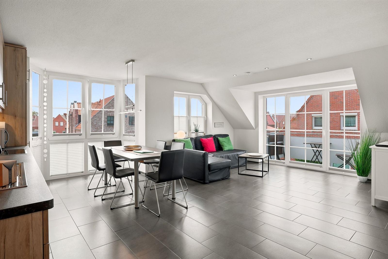 Wohn- und Essbereich mit großem Fenster, Sofa, Tisch und Blick auf Balkon.