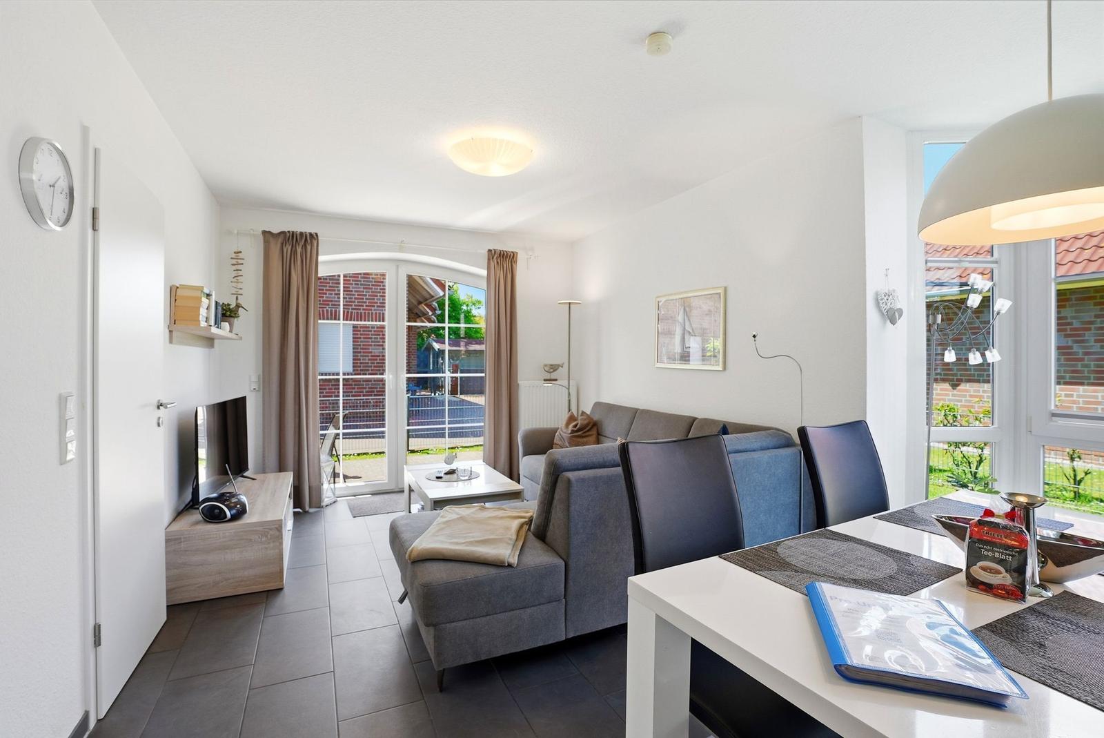 Wohn- und Essbereich mit Sofa, Esstisch und TV. Durchgang zur Terrasse mit Gartenansicht.