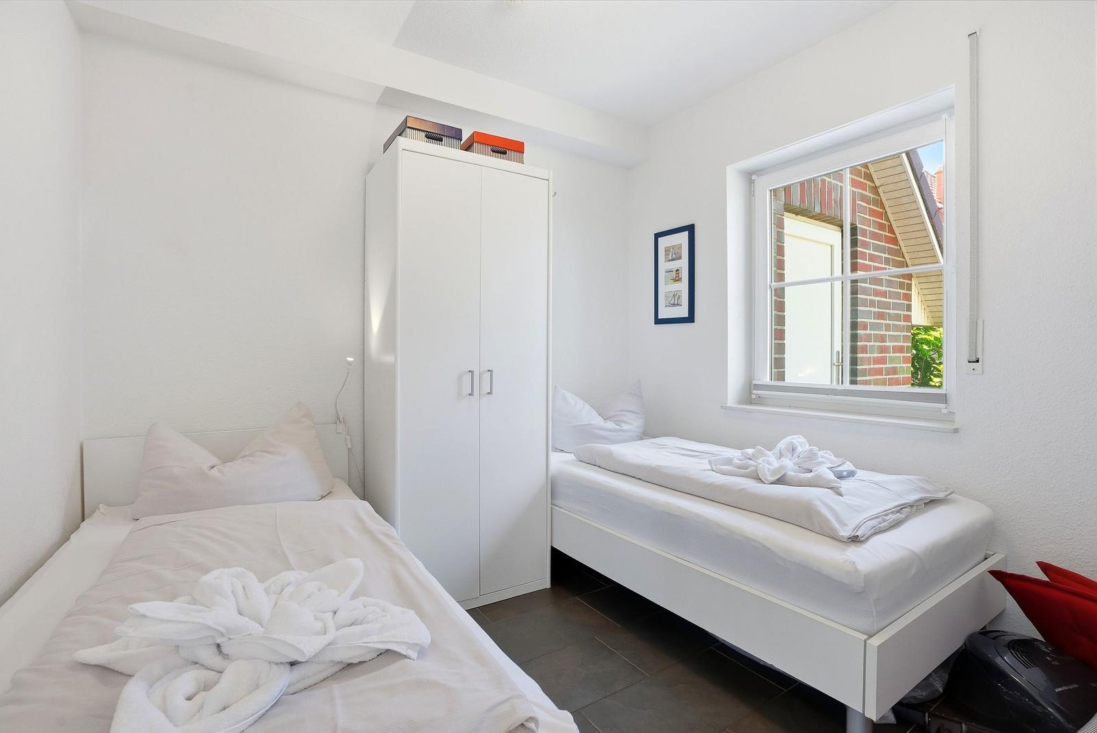 Zimmer mit zwei Betten, Schrank und Fenster. Auf Betten liegen Handtücher.