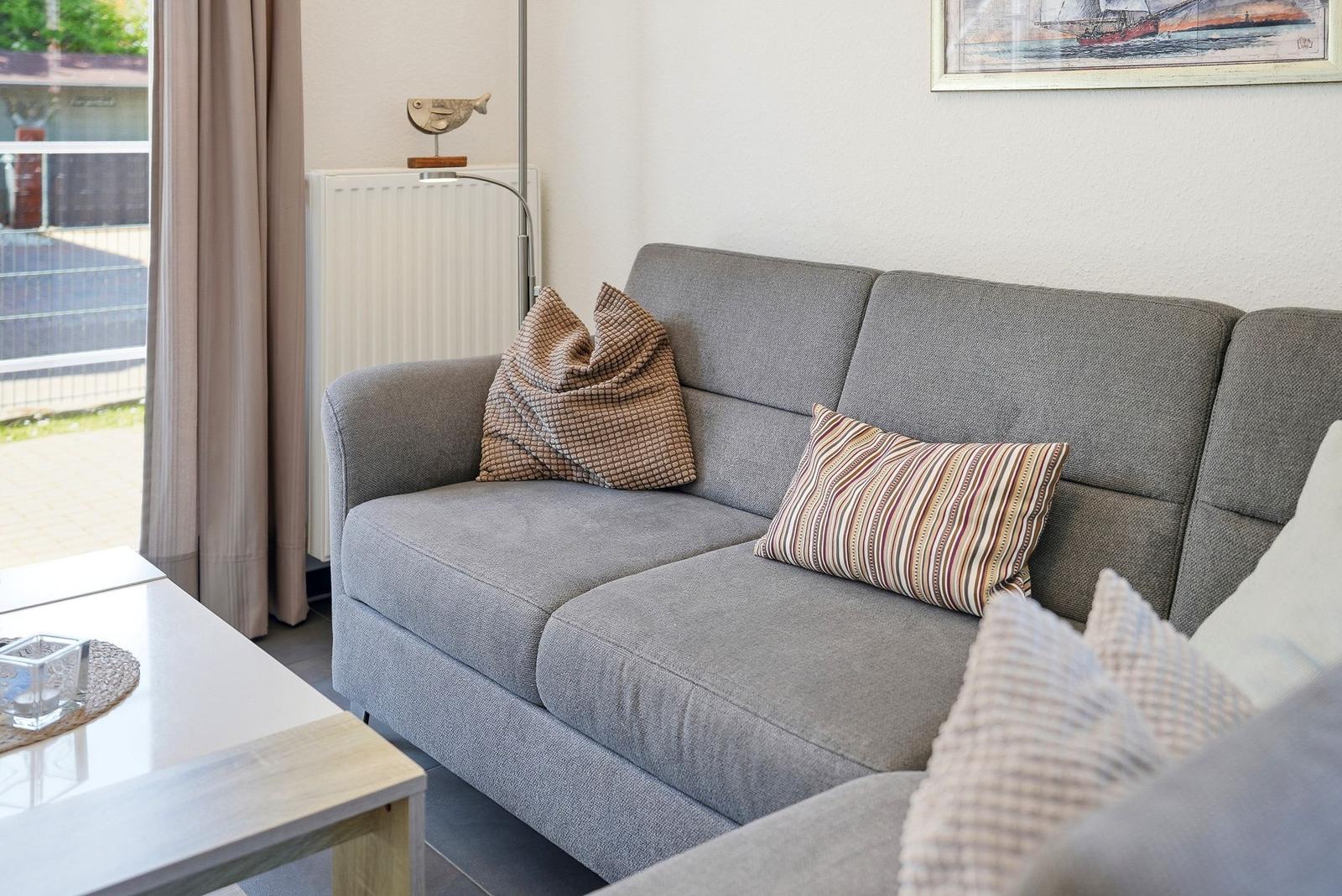 Graße Couch mit Kissen und Tisch im Wohnzimmer. Fenster mit Vorhängen und Wandbild.