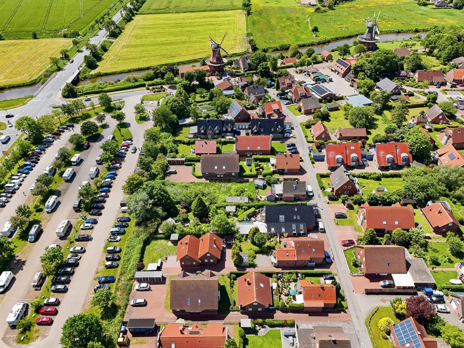 Luftbild eines Dorfes mit Häusern, Windmühlen und einem Parkplatz mit Fahrzeugen.