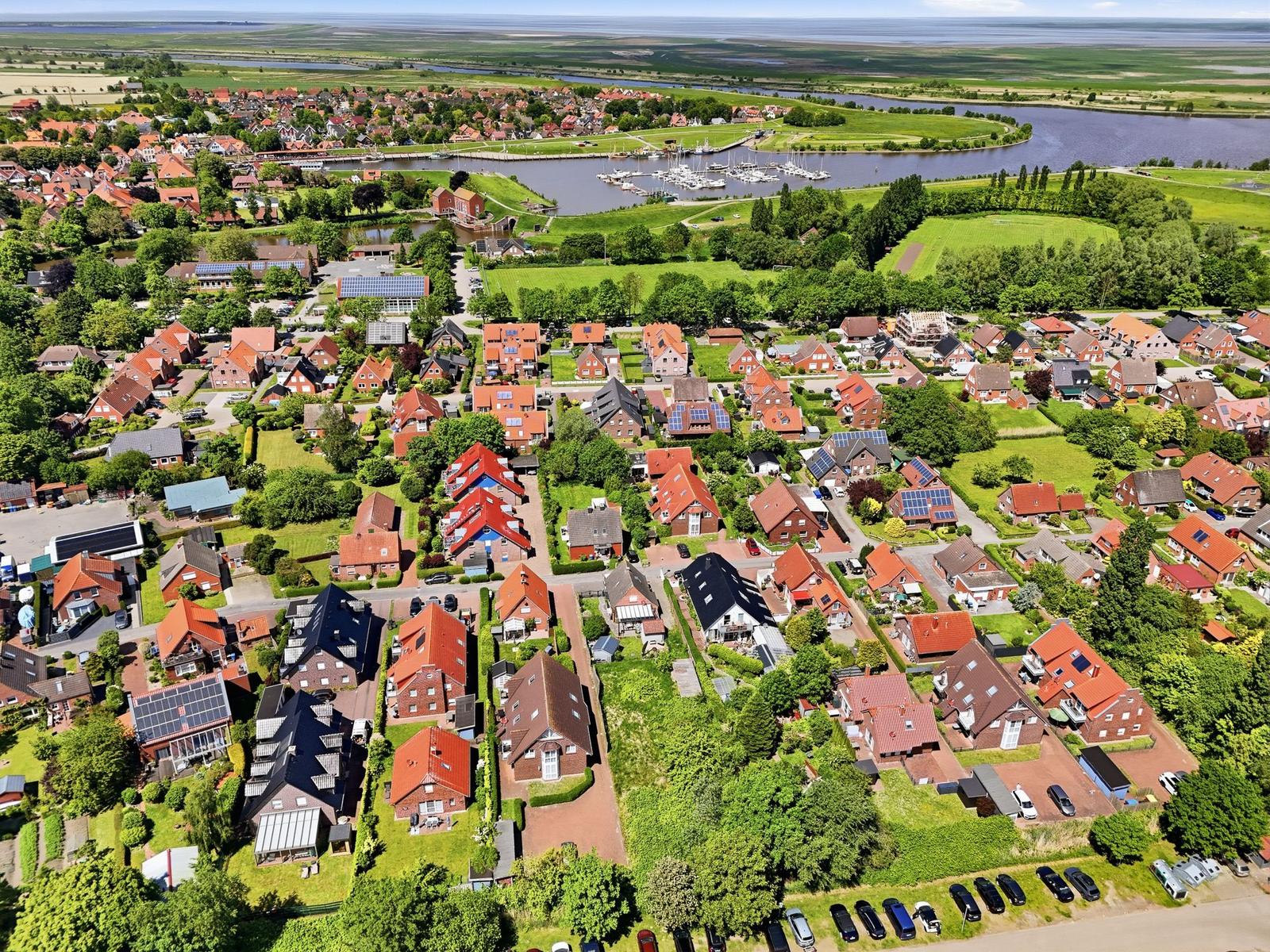 Aerial view of a village with red-roofed houses, green lawns, and a river with boats.