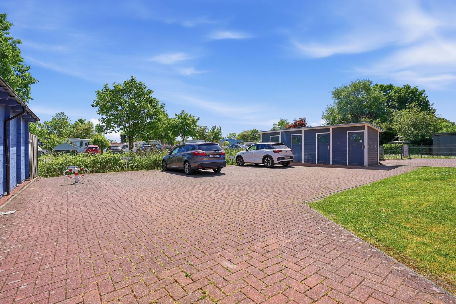 Zwei Autos stehen auf einem gepflasterten Platz vor blauen Gartenhäusern.