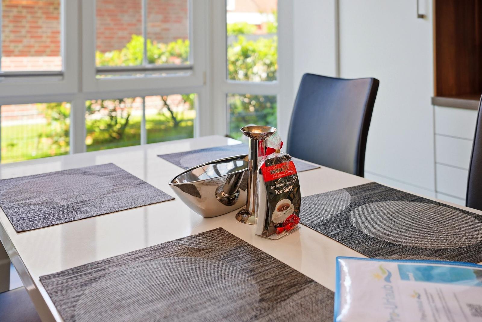 Esstisch mit Platten, Teekanne und Teebeutel vor Fenster mit Gartenblick.