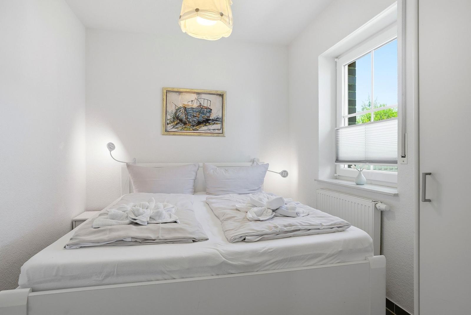 Schlafzimmer mit weißem Bett, Wandbild und Fenster mit Jalousie.