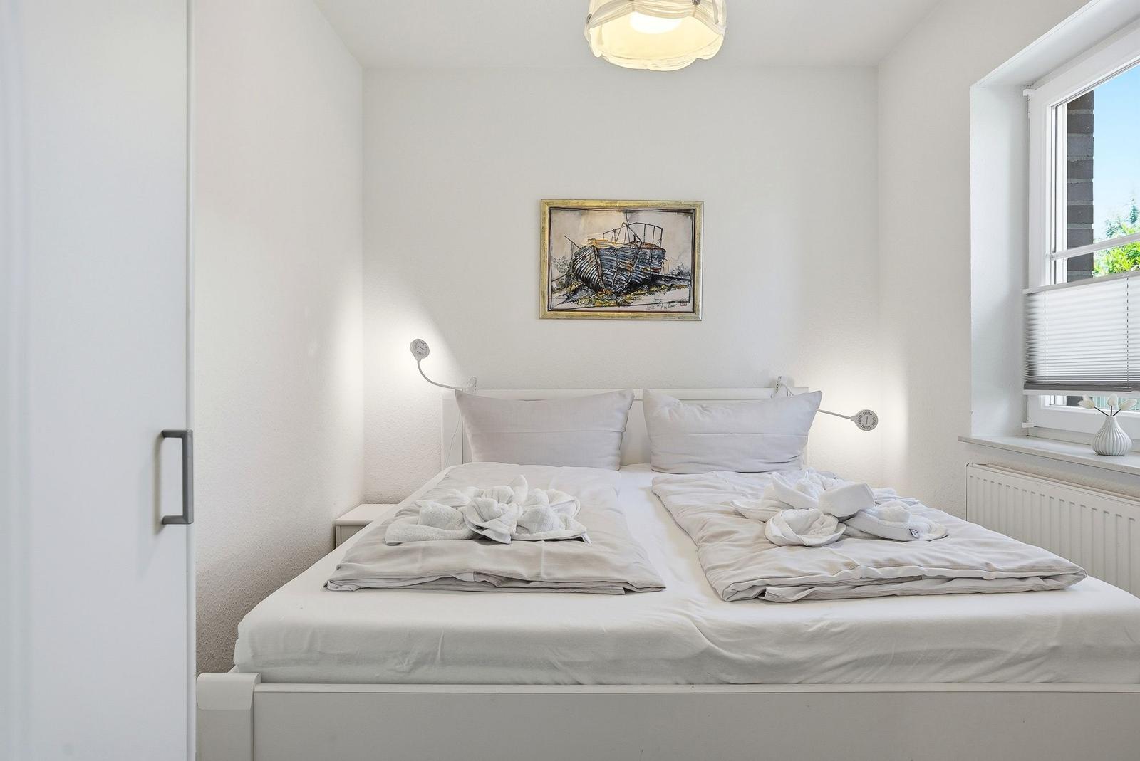 Schlafzimmer mit weißem Bett, Wandbild und Fenster mit Jalousie.