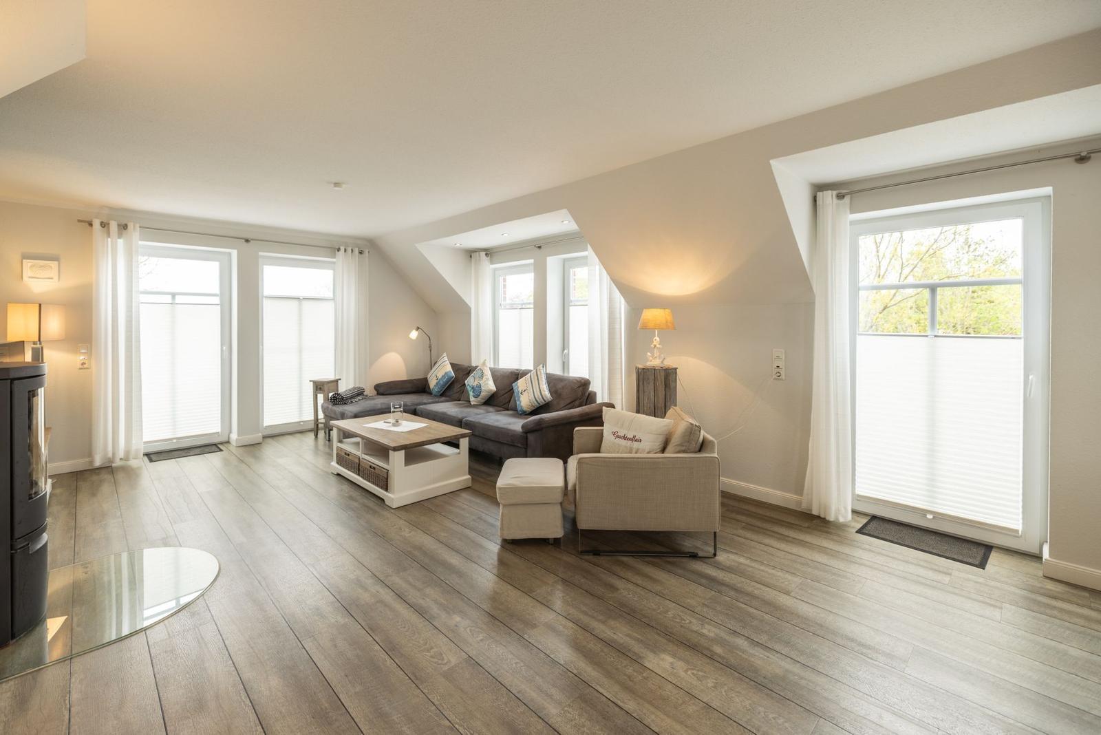 Wohnzimmer mit Holzboden, Sofa, Sessel und großen Fenstern.