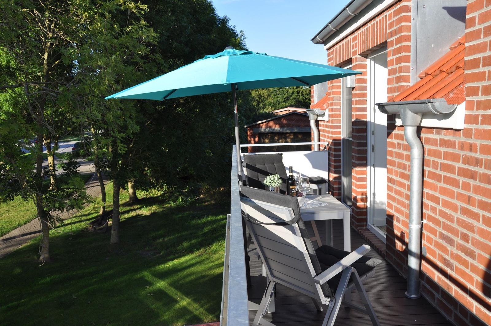 Terrasse mit Tisch, Stühlen und blauem Sonnenschirm neben rotem Backsteinhaus.