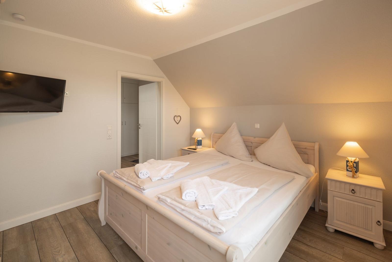 Schlafzimmer mit Doppelbett, zwei Nachttischen und Fernseher an der Wand.