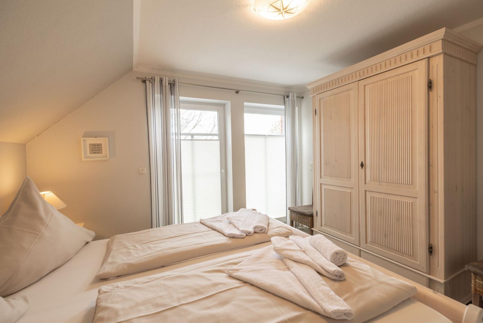 Schlafzimmer mit Doppelbett, Kleiderschrank und Fenstern mit Jalousien.