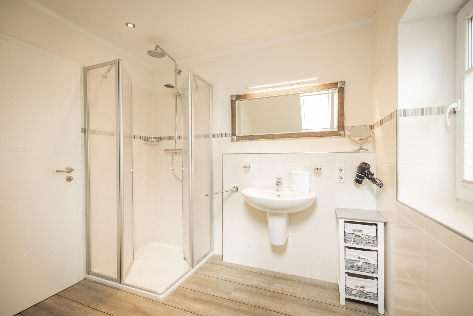 Badezimmer mit Dusche, Waschbecken und Spiegel. Holzfußboden und Fenster.