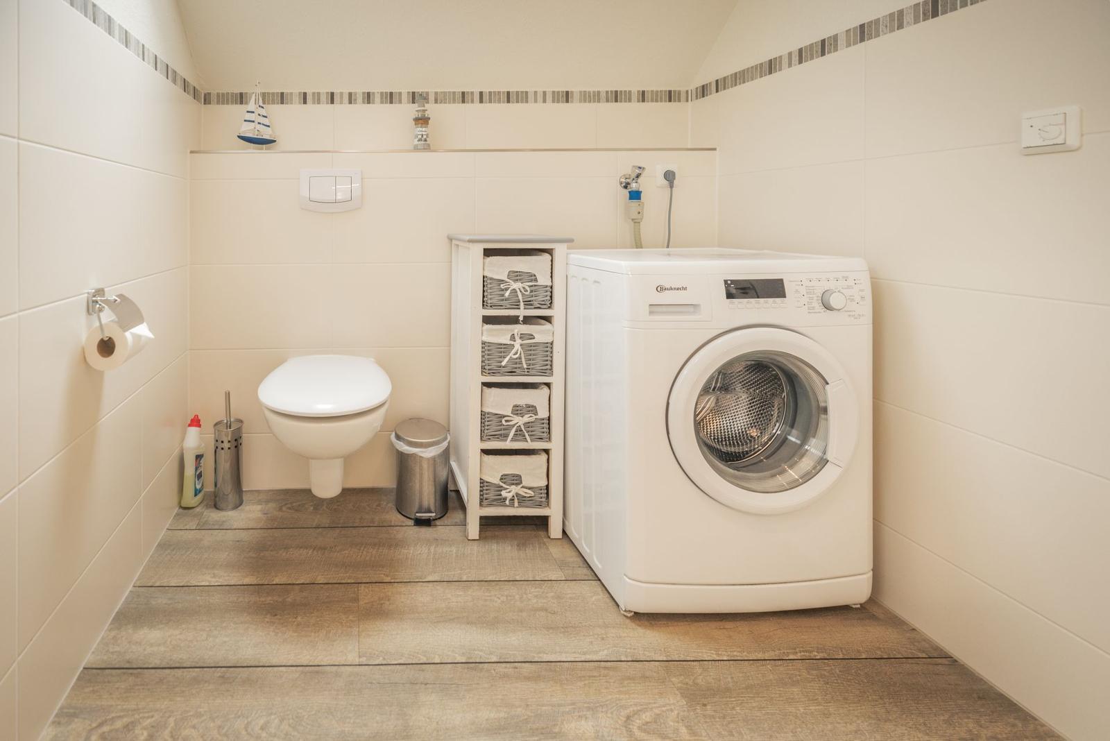 WC mit Waschmaschine, Wäscheständer und Boden aus Holzoptik.