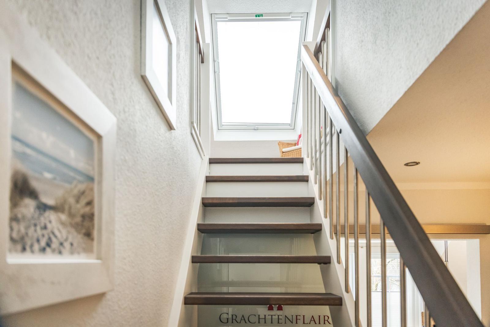 Treppe mit Holzstufen und Geländer führt zur oberen Etage. An der Wand hängen Bilder.