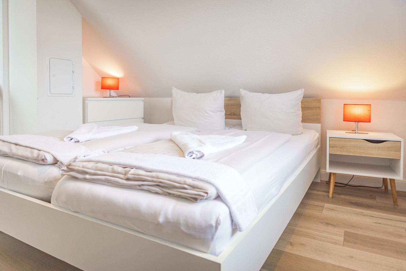 Ein Schlafzimmer mit Doppelbett, zwei Nachttischen und orangefarbenen Lampen.