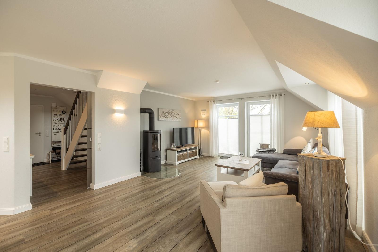 Wohnzimmer mit Holzboden, Sofa, Couchtisch und Kaminofen. Durchgang zur Treppe und Fenster.
