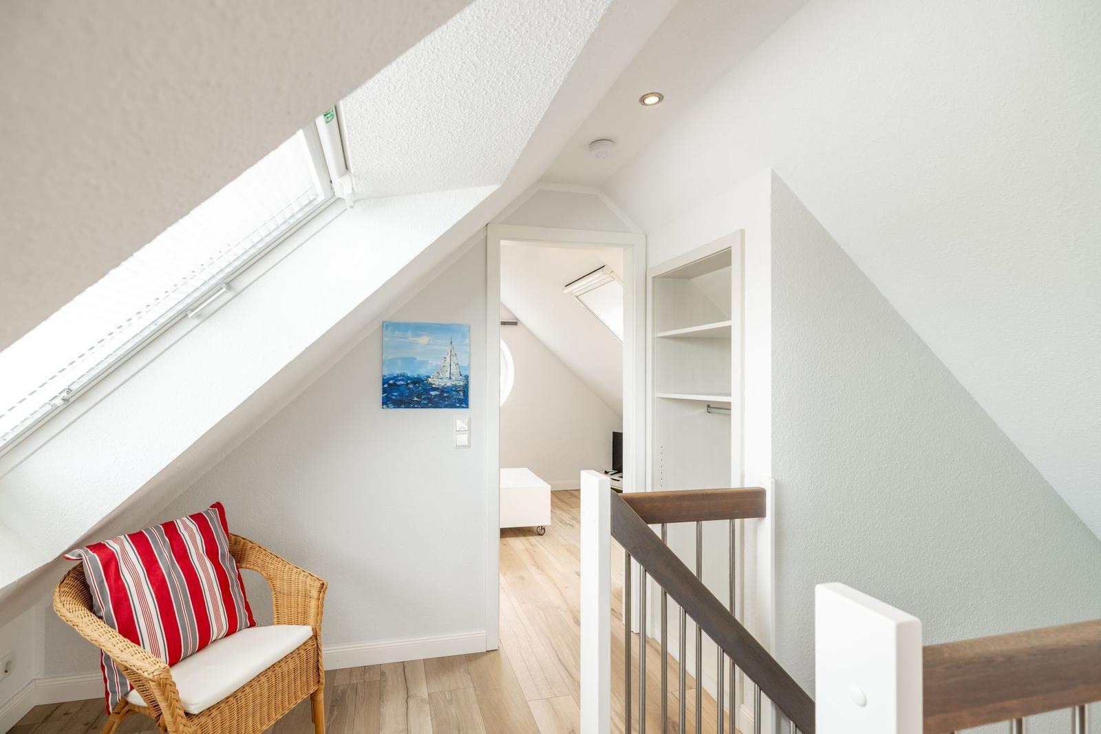 Dachgeschosszimmer mit Sitzgelegenheit, Wandbild und Blick in angrenzenden Raum.