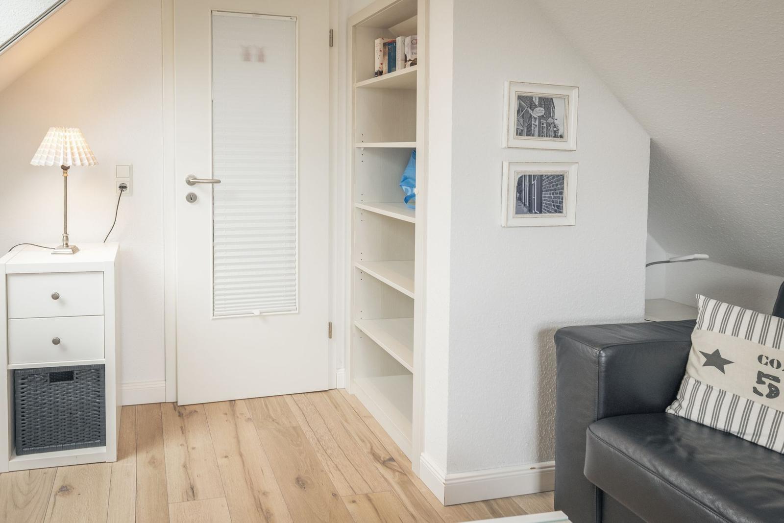 Schlafzimmer mit Schrank, Tür und Sofa. Holzboden und weiße Wände.