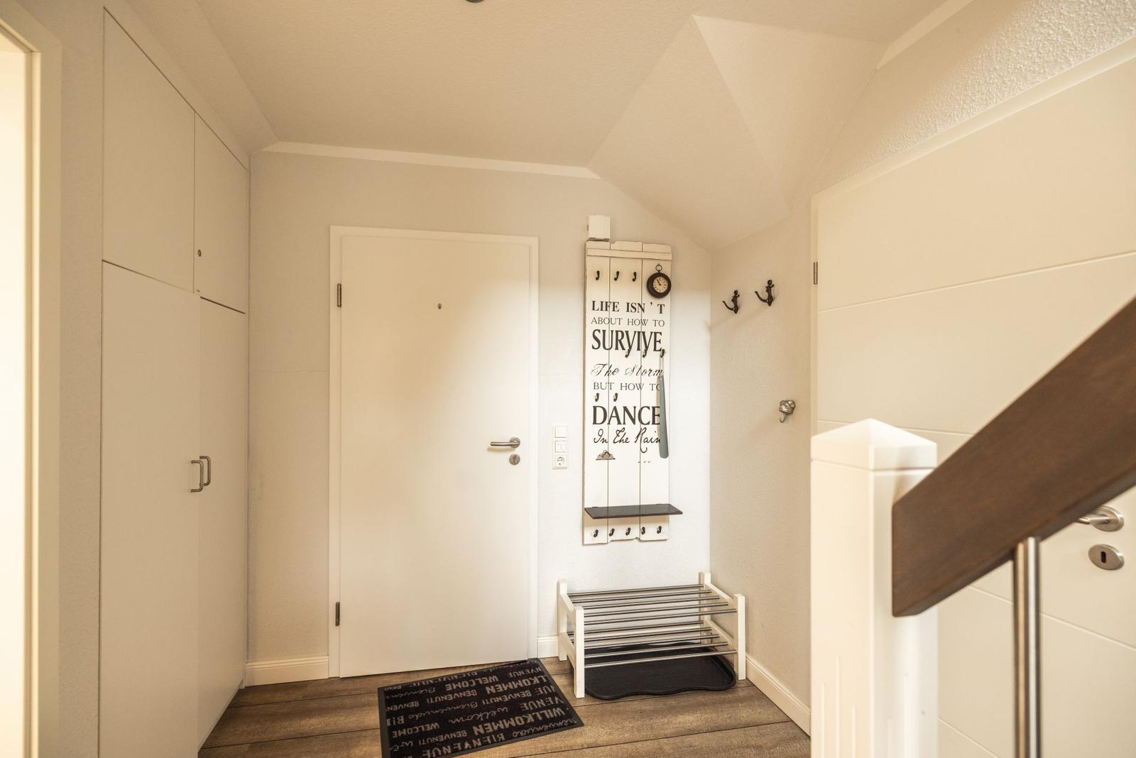 Eingangsbereich mit Garderobe, Wanduhr und Schuhregal. Holzfußboden und weiße Wände.