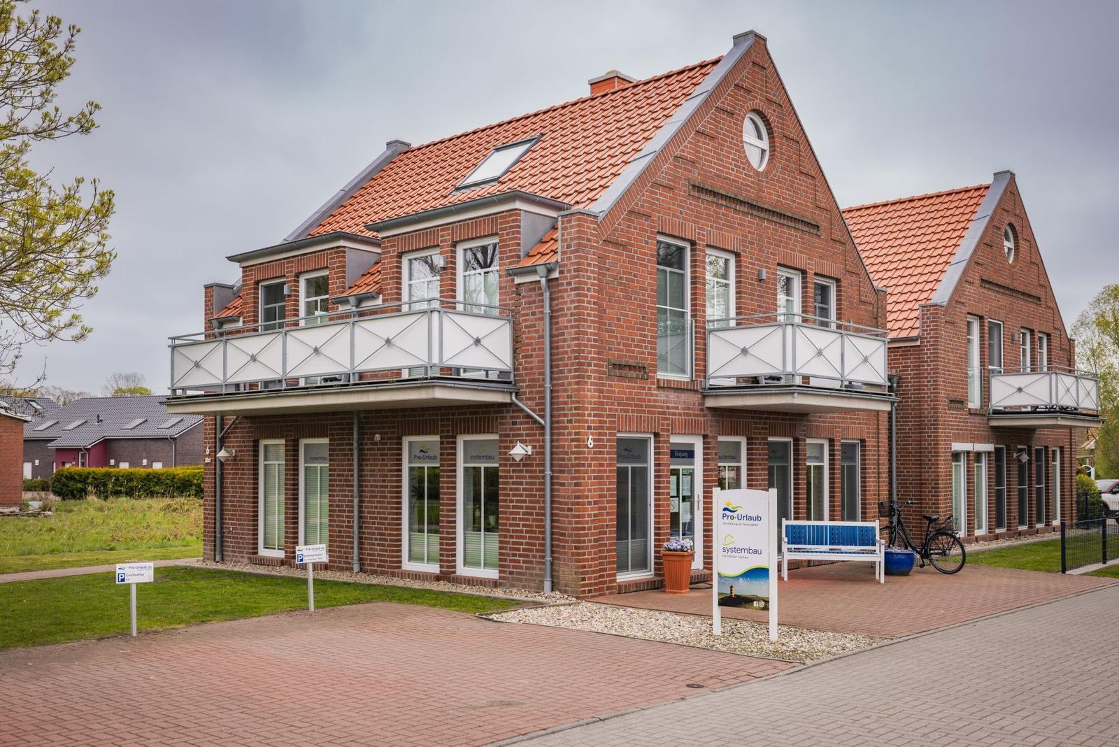 Zweistöckiges Backsteinhaus mit Balkonen und rotem Dach. Vor dem Haus steht ein Fahrrad.