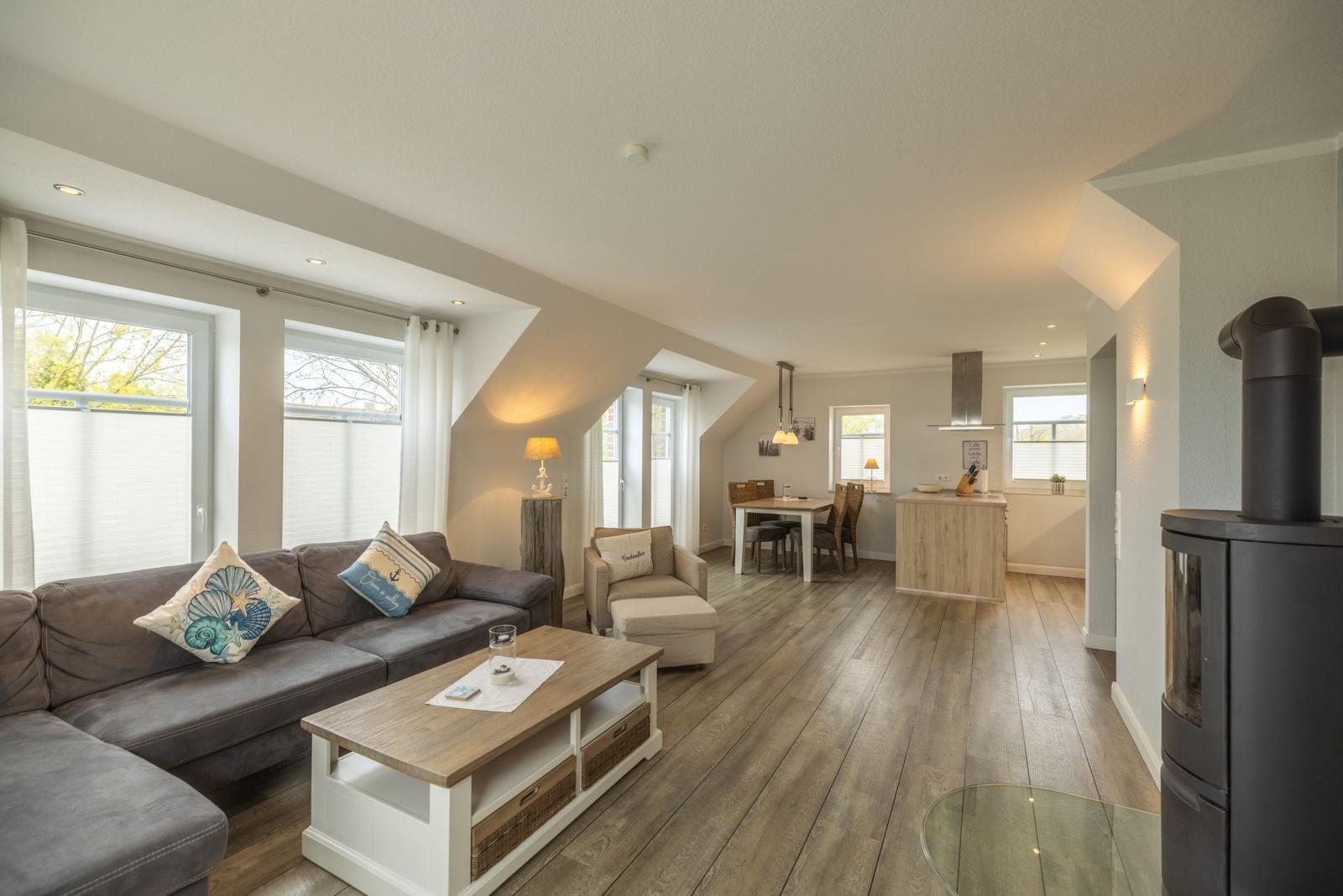 Wohn- und Essbereich mit Holzboden, Sofa, Kaminofen und Küchenzeile.