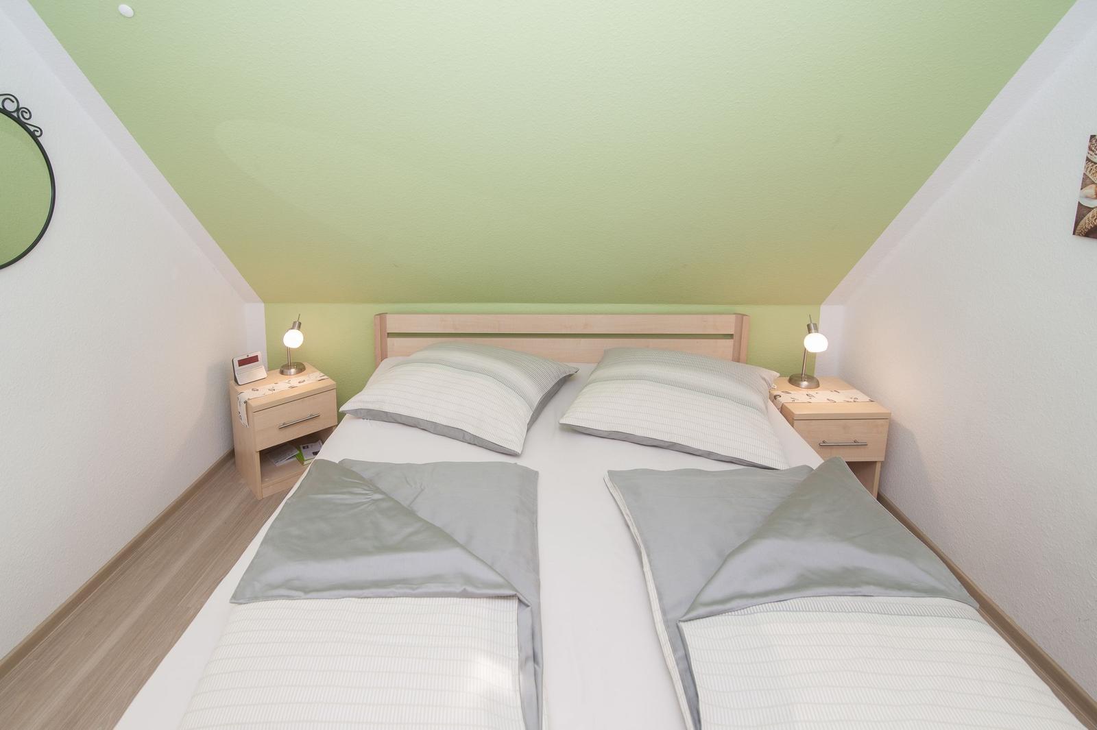 Doppelbett mit zwei Nachttischen und Lampen unter grünem Dachschrägdecken
